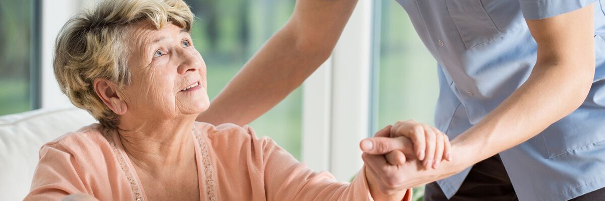 Senior woman in assisted living facility being helped by a friendly caregiver